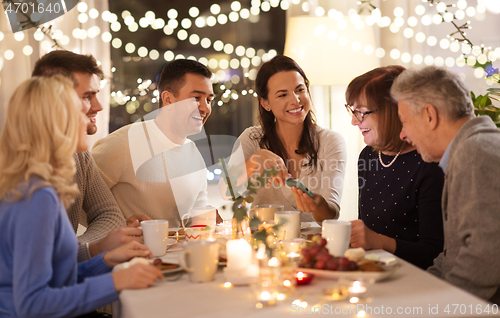 Image of happy family with smartphone at tea party at home