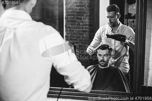 Image of Young handsome barber making haircut for attractive man in barbershop