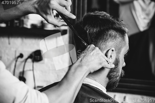 Image of Young handsome barber making haircut for attractive man in barbershop