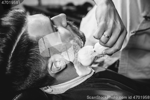 Image of Client during beard shaving at barbershop.