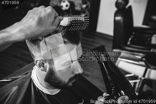 Image of Young handsome barber making haircut for attractive man in barbershop