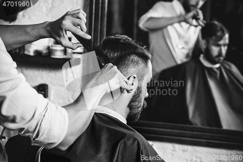 Image of Young handsome barber making haircut for attractive man in barbershop