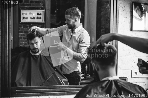 Image of Young handsome barber making haircut for attractive man in barbershop