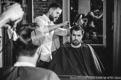 Image of Young handsome barber making haircut for attractive man in barbershop