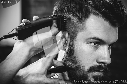 Image of Young handsome barber making haircut for attractive man in barbershop