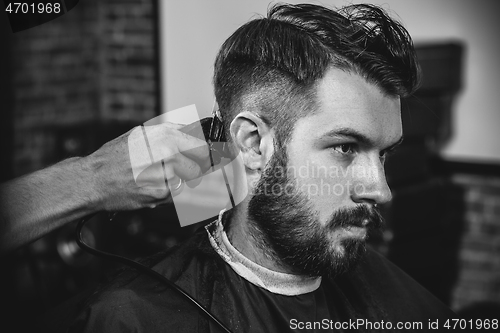Image of Young handsome barber making haircut for attractive man in barbershop