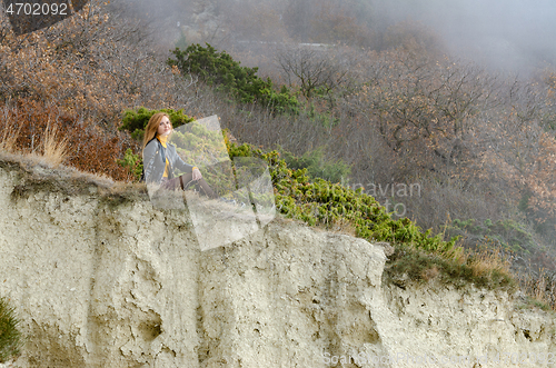 Image of A girl sits on a hillock in the mountains and enjoys a wonderful view