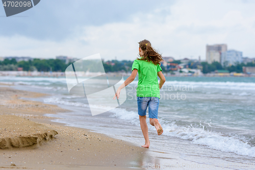 Image of A girl happily runs along the sea coast, view from the back