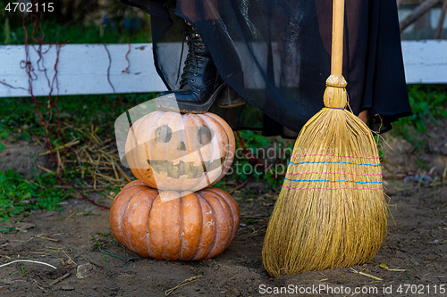 Image of On a pumpkin with a drawn scary face is a witch\'s foot, next to a broom, close-up
