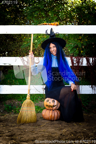 Image of A girl in a witch costume sits on two pumpkins and holds a broom in her hands