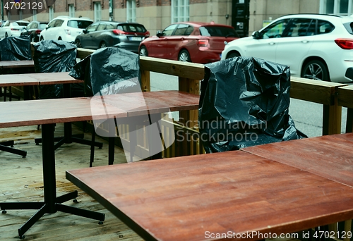 Image of summer is over, plastic-covered chairs in empty street cafe