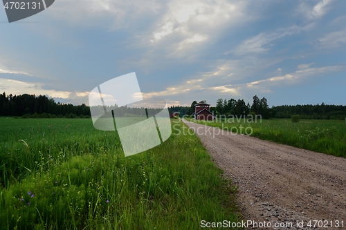 Image of field, dirt road and two red barns in Finland