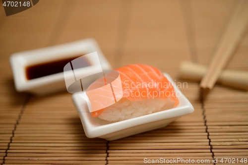 Image of chopsticks, soy sauce and sushi with salmon on the mat