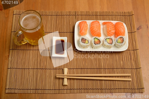 Image of chopsticks, soy sauce, sushi and glass of beer on the mat