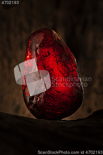 Image of Beauty of natural raw amber. A piece of dark red semi transparent natural amber on piece of stoned wood.