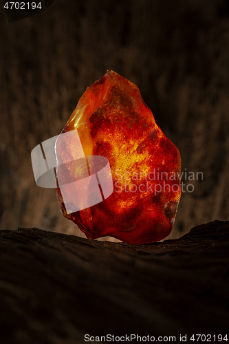 Image of Beauty of natural raw amber. A piece of yellow and red semi transparent natural amber on piece of stoned wood.