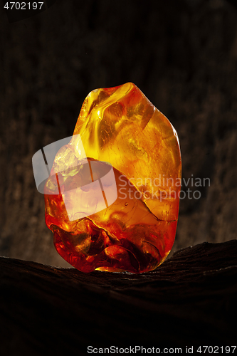 Image of Beauty of natural raw amber. A piece of yellow opaque natural amber on large piece of dark stoned wood.