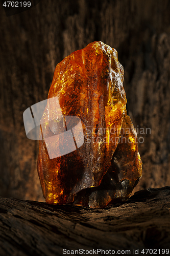 Image of Beauty of natural raw amber. A piece of yellow opaque natural amber on large piece of dark stoned wood.