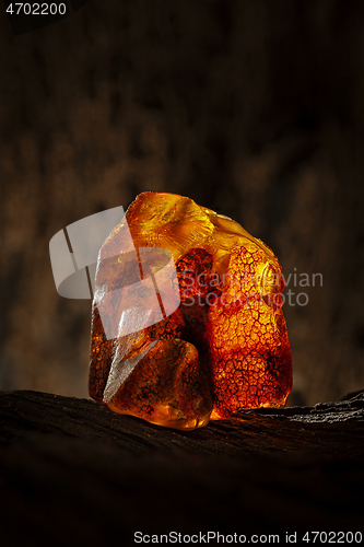 Image of Beauty of natural raw amber. A piece of yellow and red semi transparent natural amber on piece of stoned wood.