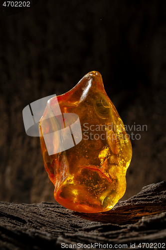 Image of Beauty of natural raw amber. A piece of yellow opaque natural amber on large piece of dark stoned wood.