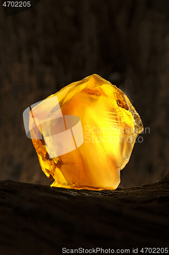 Image of Beauty of natural raw amber. A piece of yellow opaque natural amber on large piece of dark stoned wood.