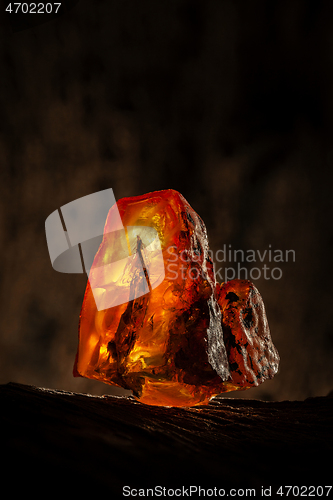 Image of Beauty of natural raw amber. A piece of yellow-red transparent natural amber on piece of stoned wood