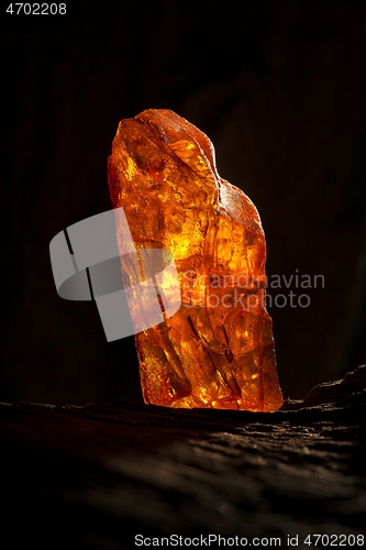 Image of Beauty of natural raw amber. A piece of yellow-red transparent natural amber on piece of stoned wood