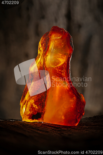 Image of Beauty of natural raw amber. A piece of yellow-red transparent natural amber on piece of stoned wood