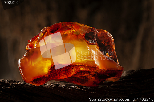 Image of Beauty of natural raw amber. A piece of yellow-red transparent natural amber on piece of stoned wood