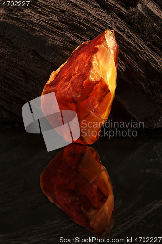 Image of Beauty of natural raw amber. A piece of yellow-red transparent natural amber on piece of stoned wood