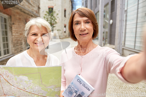 Image of senior women with map and city guide taking selfie