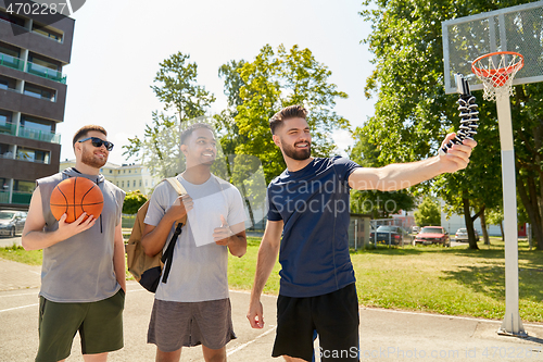 Image of happy men taking selfie on basketball playground