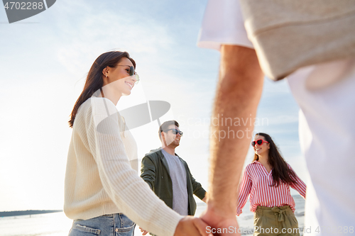 Image of happy friends holding hands on summer beach