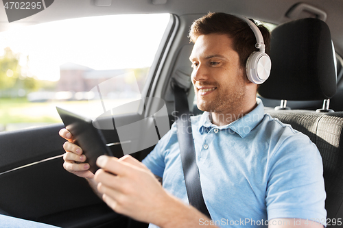 Image of passenger in headphones with tablet pc in taxi car