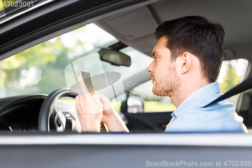 Image of man driving car and using smartphone