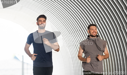 Image of two happy young male friends running outdoors