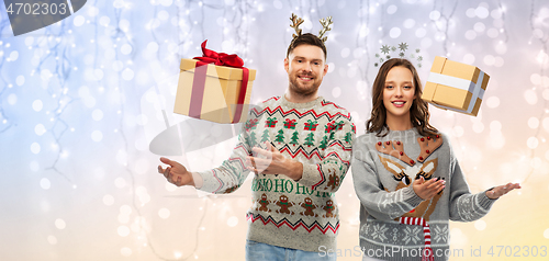 Image of happy couple in christmas sweaters with gift boxes