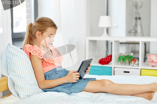 Image of smiling girl with tablet pc sitting on bed at home