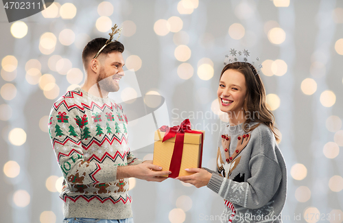 Image of happy couple in ugly sweaters with christmas gift