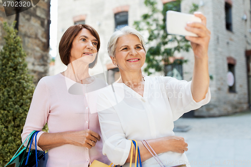 Image of old women with shopping bags taking selfie in city