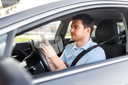 Image of man driving car and using smartphone