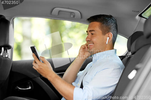 Image of passenger with earphones and cellphone in taxi car