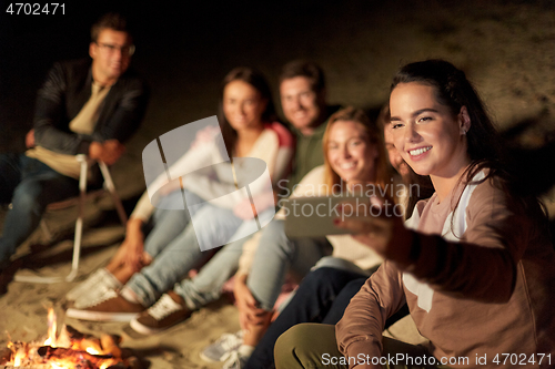 Image of happy friends taking selfie at camp fire on beach
