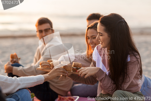 Image of happy friends eating sandwiches at picnic on beach