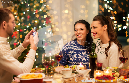 Image of happy friends photographing at christmas dinner