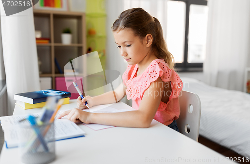 Image of student girl with book writing to notebook at home