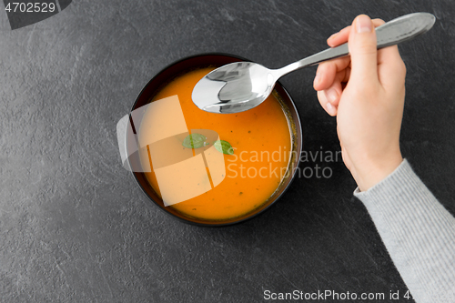 Image of hands with bowl of pumpkin cream soup on table