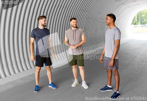 Image of young sporty men or male friends talking in tunnel