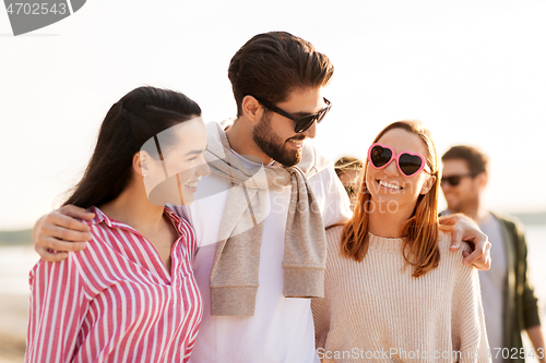 Image of happy friends walking along summer beach