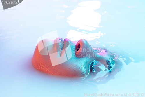 Image of Beautiful female face in the milk bath with soft glowing in blue-pink neon light